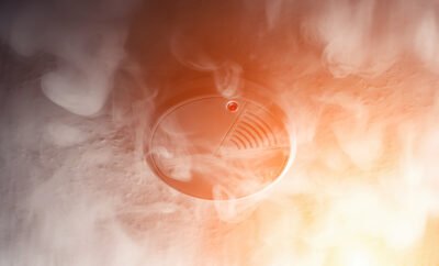 Photo of a smoke detector with smoke and red light to depict danger from fire and the importance of smoke alarms that work